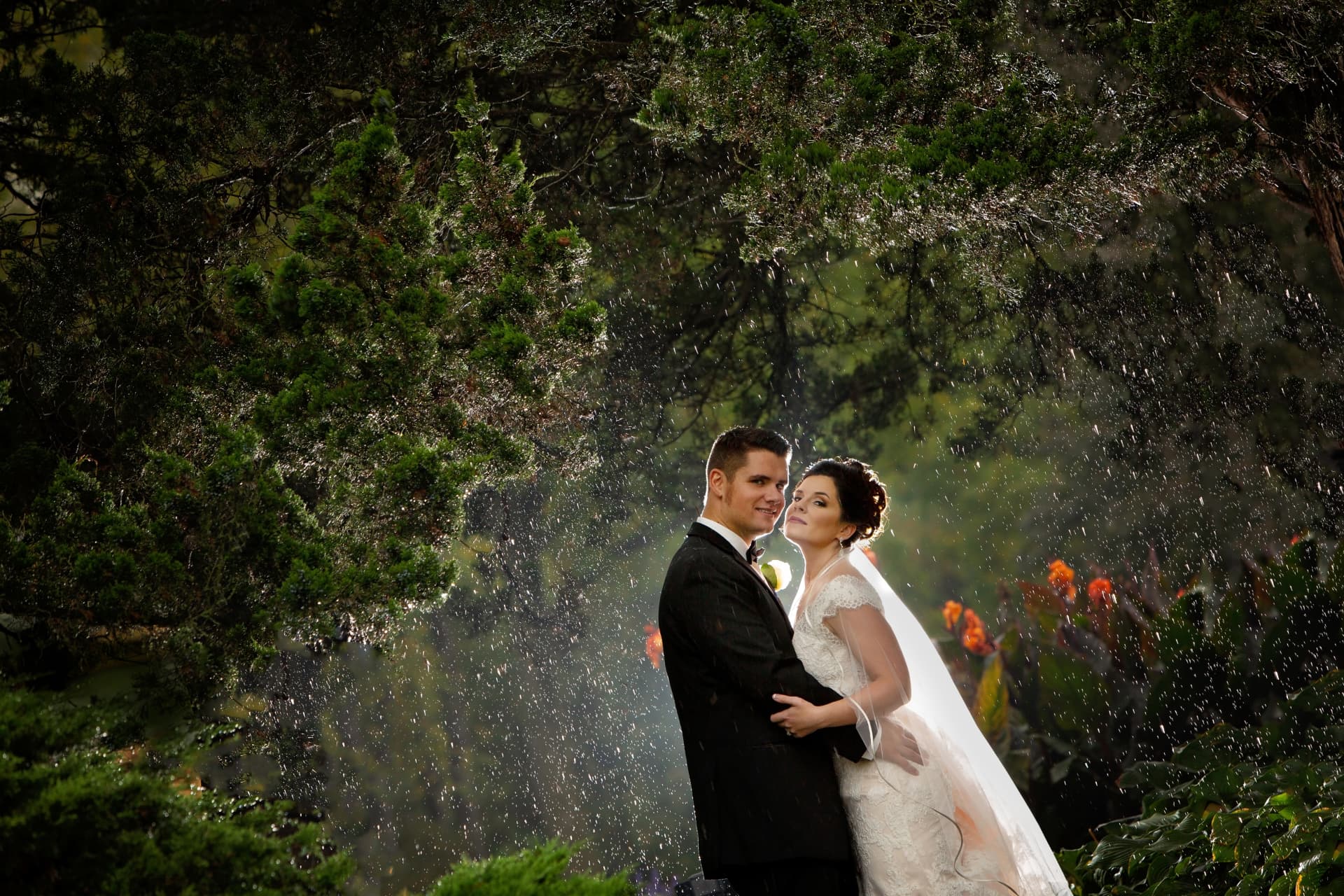 Bride and groom embracing in the rain surrounded by lush greenery